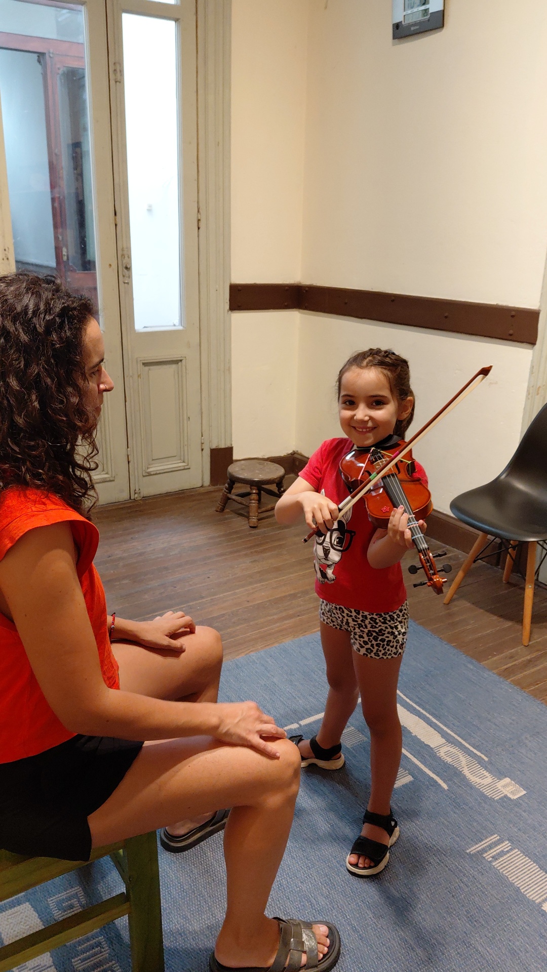 Pequeña alumna con violín sonriendo junto a su profesora