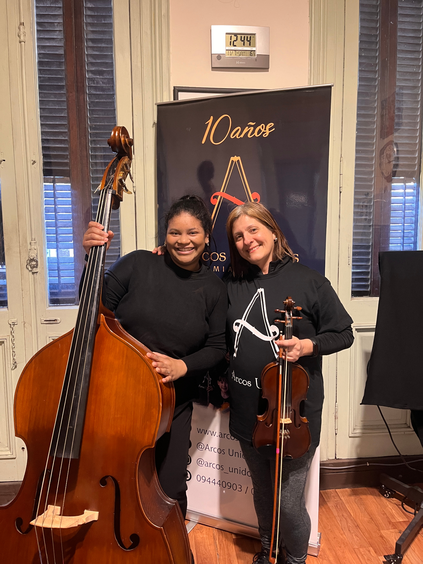 Alumna con contrabajo y profesora con violín frente al banner de los 10 años