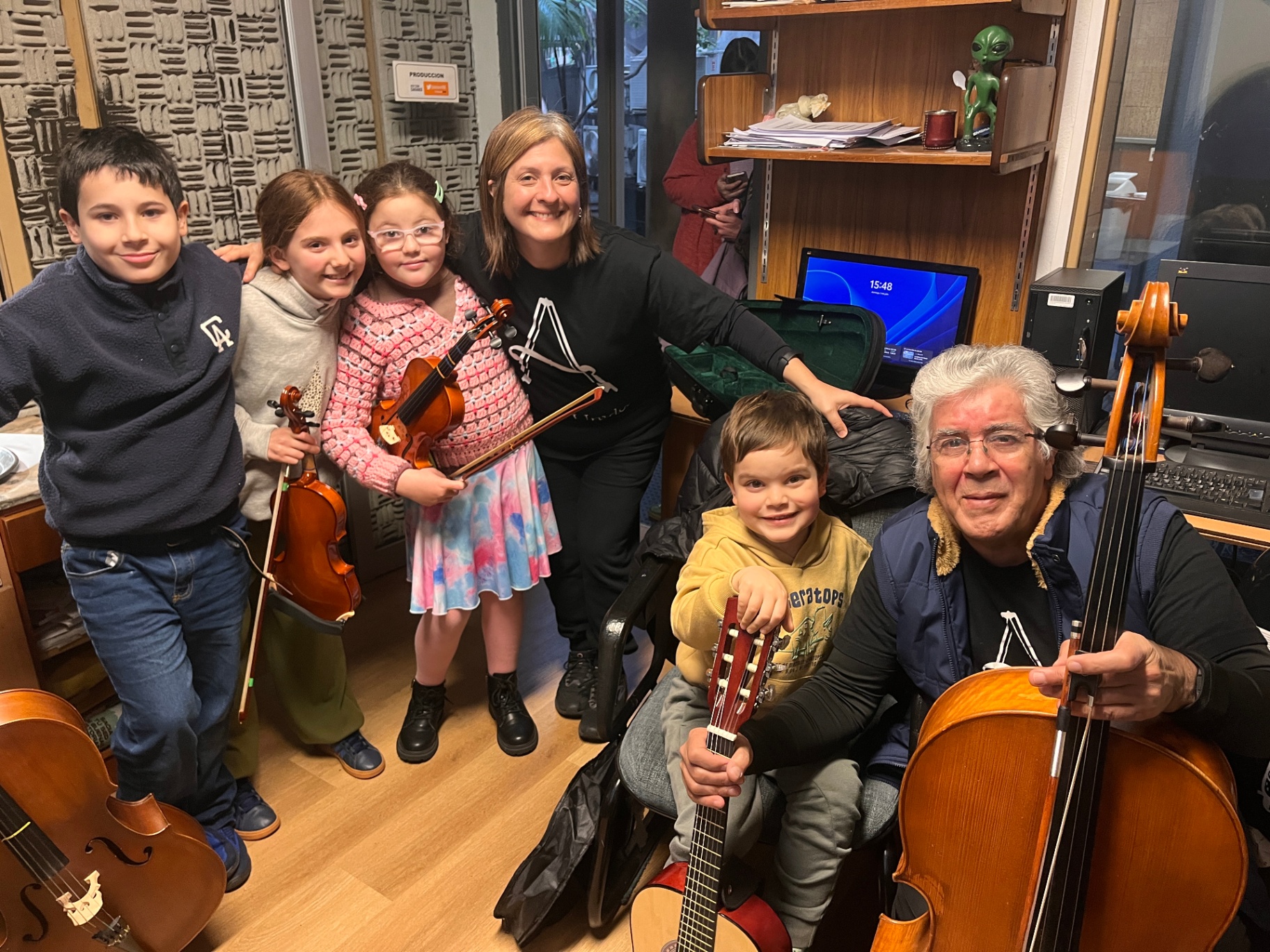 Grupo de estudiantes y profesor con violines, guitarra y cellos en el aula